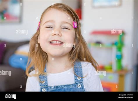 Portrait Of Three Years Old Blonde Girl With Blue Jeans Dress Or Dungarees Standing Indoor