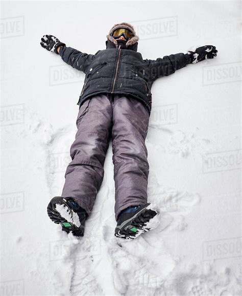 Boy lying on back on snow-covered ground - Stock Photo - Dissolve