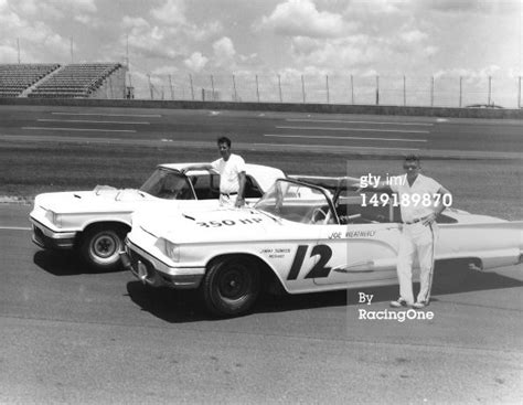 Two Men Standing Next To An Old Race Car On The Tarmac In Black And White