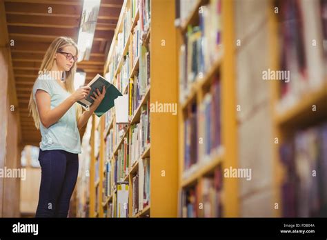 Blonde Student Reading Book Next To Bookshelf Stock Photo Alamy