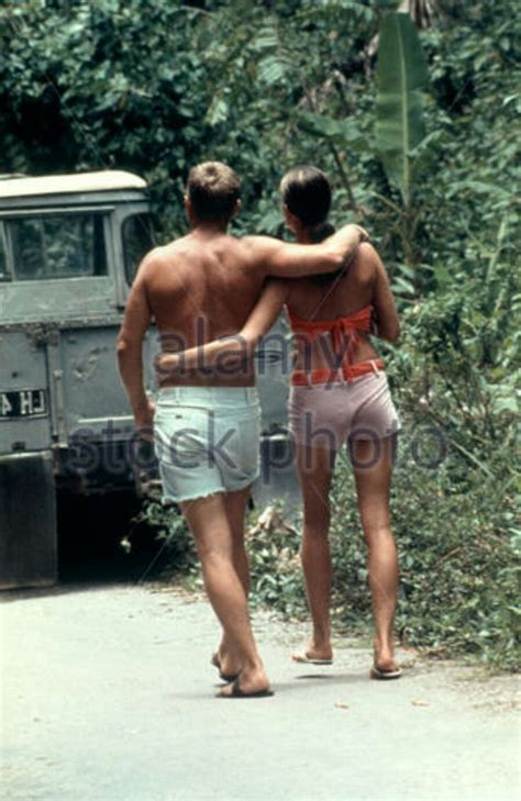 Two People Walking Down The Road In Front Of An Army Truck With No Shirt On