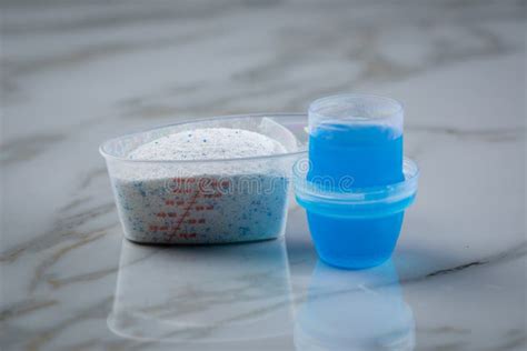 Laundry Detergent Powder And Blue Liquid Gel In Measuring Cup Stock