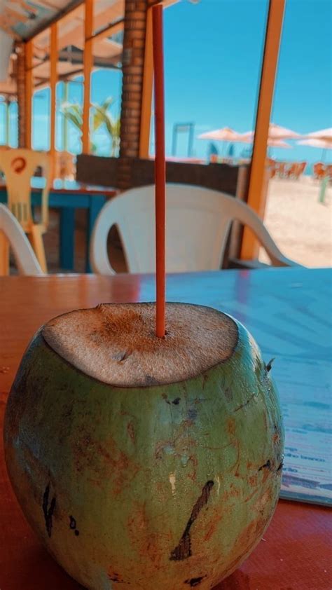 A Green Coconut Drink Sitting On Top Of A Wooden Table Next To Chairs