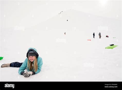 Smiling Young Girl Lying Down At The Bottom Of Snowy Sledding Hill