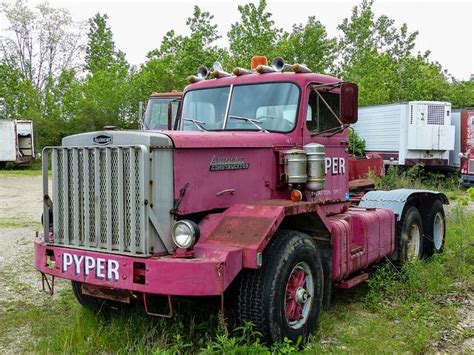 An Old Pink Truck Is Parked In The Grass Next To Some Other Trucks And