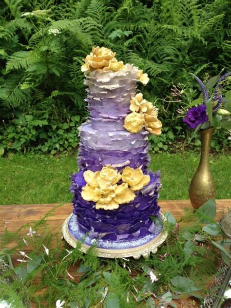 A Purple And Yellow Tiered Cake Sitting On Top Of A Table Next To Flowers