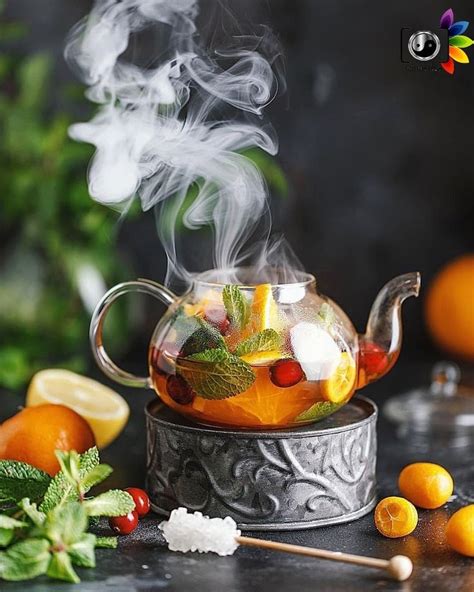 A Tea Pot Filled With Fruit And Ice On Top Of A Table Next To Oranges