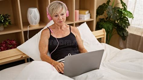 A Mature Woman With Grey Hair Relaxing In Bed With Headphones And A