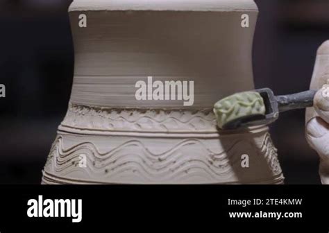 The Male Hands Of A Potter Carve Designs On A Soft White Clay Pot Using