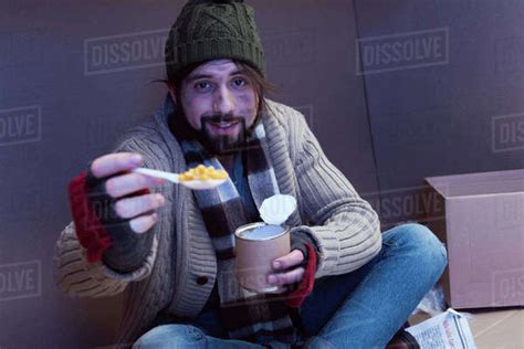 Smiling Homeless Man Eating Canned Food In Cardboard Box Stock Photo