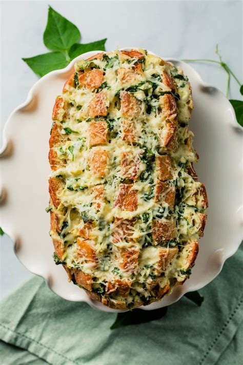 A White Plate Topped With Bread Covered In Cheese And Spinach Toppings On Top Of A Green Napkin