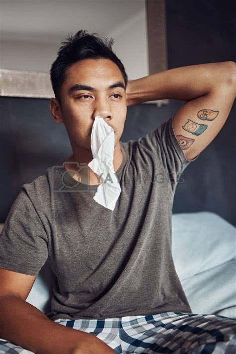 A Man Sitting On A Bed With A Napkin In His Mouth And Hand Over His Nose