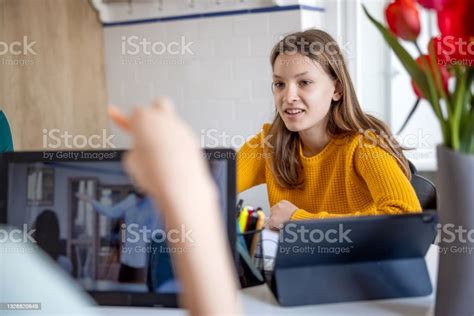 Teenage Girl Sitting At Home And Doing Homework Distracting Her Sister