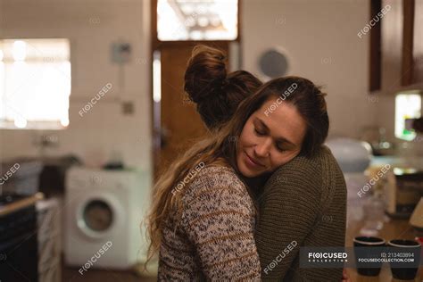 Lesbian Couple Hugging In Kitchen At Home Lock Down Closeness Stock Photo