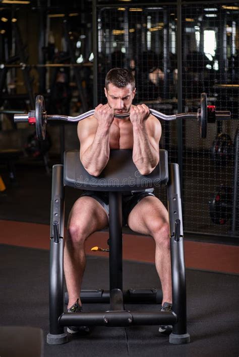 Muscular Man Sitting On The Bench And Doind Biceps Exercise Stock Image