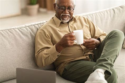 An Older Man Sitting On A Couch Holding A Coffee Cup And Looking At His