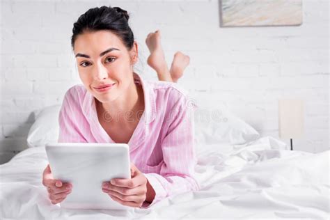 Portrait Of Smiling Woman In Pajamas With Tablet While Lying On Bed