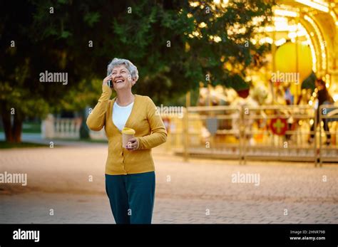 Pretty Granny With Cup Of Coffee Using Mobile Phone In Summer Park