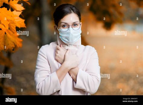 A Young Woman In A Face Mask Holds Her Hands On Her Chest Closing Her