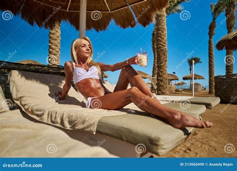 Woman Wearing Bikini Sitting On Lounger Under Straw Canopy Umbrella At