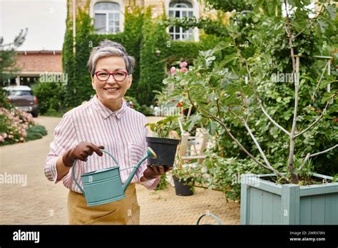 Appealing Joyful Mature Woman Holding Watering Can And Pot With Plant