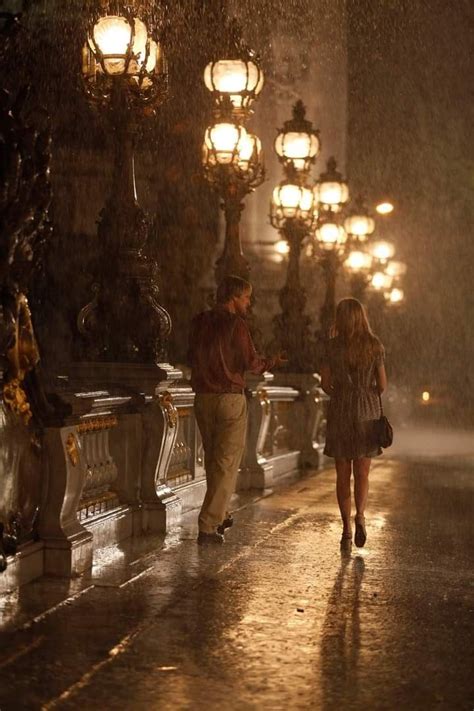 A Man And Woman Walking In The Rain Under Street Lamps With Their Backs