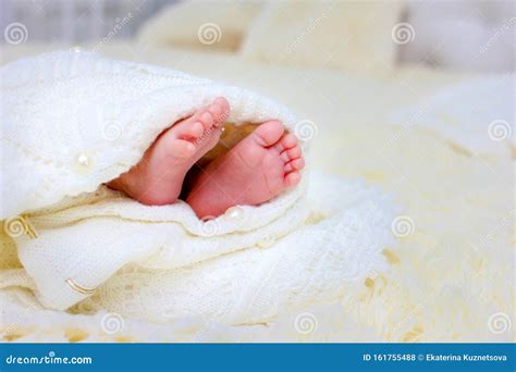 The Legs Of A Newborn Baby Wrapped In A White Warm Blanket Lying On Her