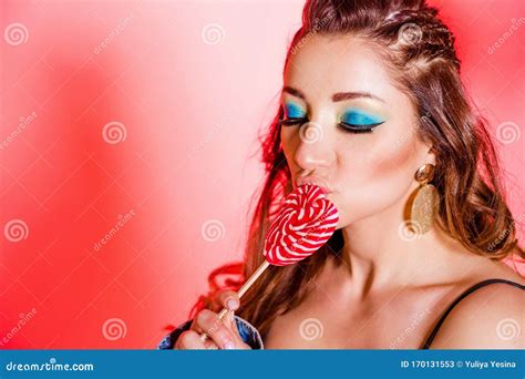 Beautiful Brunette Girl With Blue Makeup Pigtails And A Black Top Posing Against A Red