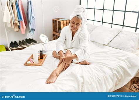 Middle Age Grey Haired Woman Caring Skin Legs Using Hydration Cream Sitting On The Bed At