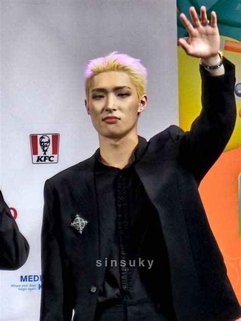 A Male In A Black Suit And Pink Hair Is Holding His Hand Up To The Sky