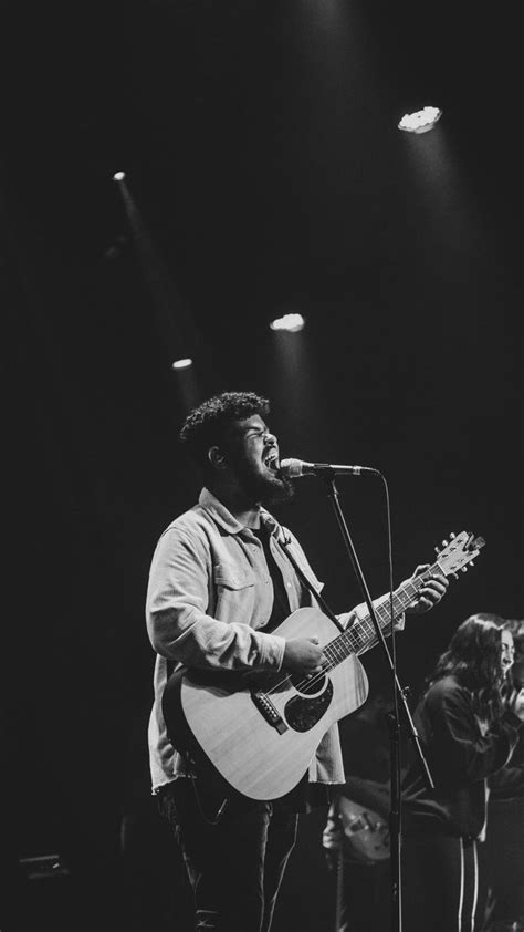 A Man With A Guitar Standing In Front Of A Microphone And Singing Into