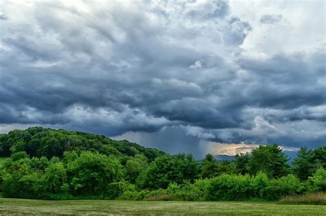 Un cielo nublado sobre un campo con árboles y montañas al fondo Foto