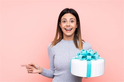 Premium Photo Woman Holding A Big Cake Over Isolated Pink Wall Surprised And Pointing Finger