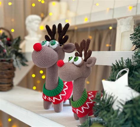 Two Knitted Reindeers Standing Next To Each Other On Top Of A White Shelf