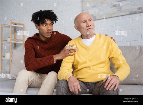 African American Grandson Hugging Disappointed Grandpa On Couch At Home