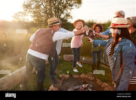 Group Of Mature Friends Making Toast As They Sit Around Fire And Sing