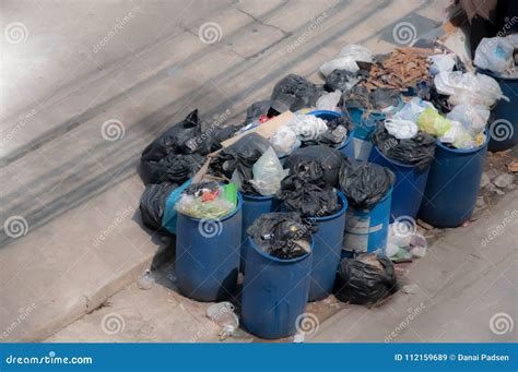 Garbage Against Full Trash Cans With Rubbish Bags Overflowing On Stock