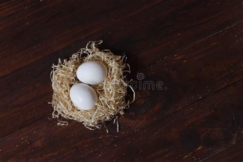 Dois Ovos De Galinha Brancos Num Ninho De Palha Numa Mesa Marrom Foto