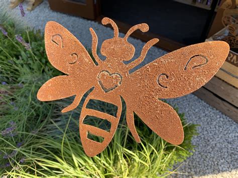 A Metal Bee Sitting On Top Of A Green Plant In Front Of A Wooden Box