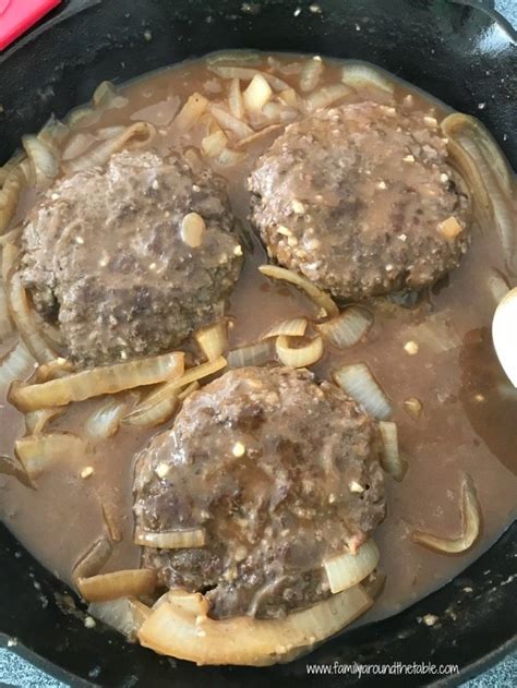 Two Hamburger Patties Are Being Cooked In A Skillet With Onions And Gravy