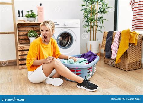 Young Caucasian Woman Putting Dirty Laundry Into Washing Machine Angry