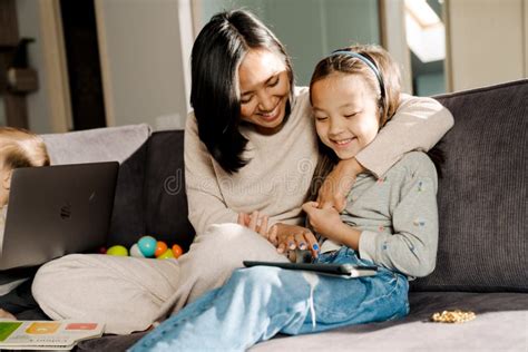 Happy Mother Using Tablet Computer While Hugging Her Daughter Stock