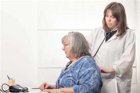 Young Female Doctor Auscultating Her Patients Back With A Stethoscope