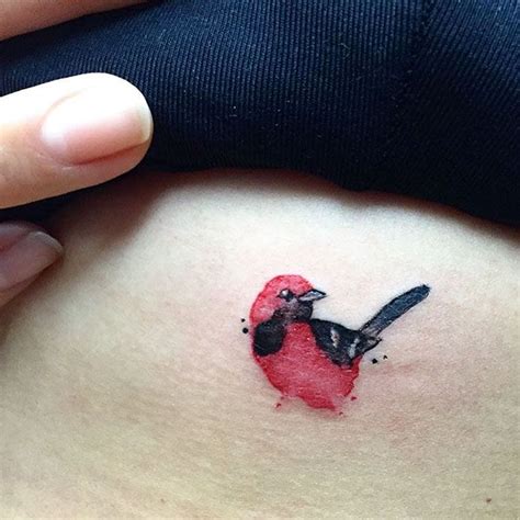 A Small Bird Tattoo On The Side Of A Womans Stomach It Is Red And Black