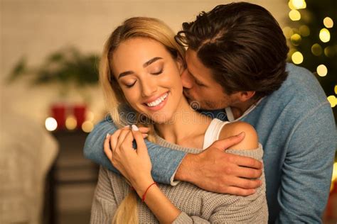 Man Kissing Neck Of Stunning Woman Sitting Near Christmas Tree Stock