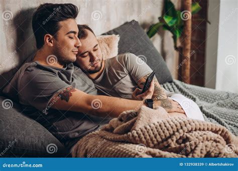 Pares Gay Felices Que Mienten Junto En Cama Y Que Usan El Smartphone Mirando Las Fotos Imagen