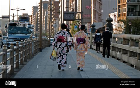 2 Geisha Girls Walk Down A Busy Street Dressed In Their Traditional