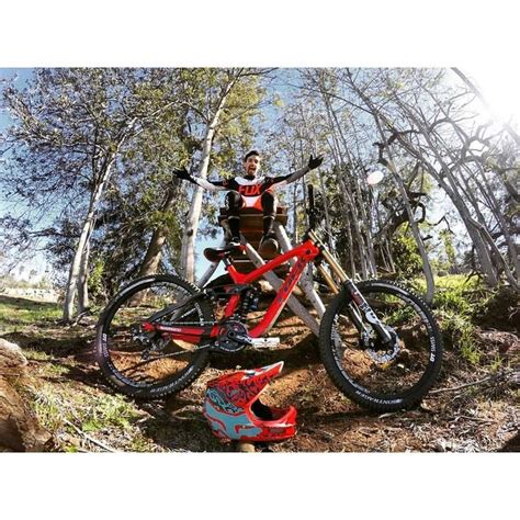 A Man Standing On Top Of A Red Bike In The Woods With His Arms Outstretched