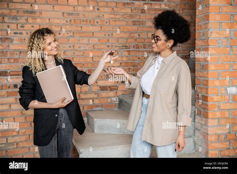 Positive Blonde Real Estate Agent With Folder Giving Keys From New