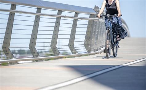 Woman Amateur Cyclist In A Skirt And Tank Top Takes A Bike Ride Along A Dedicated Bike Path On A